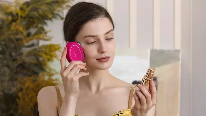 A young woman with sleek dark hair in yellow dress using FOREO BEAR 2 microcurrent device and conductive SUPERCHARGED serum 
